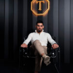 lia Topuria sentado en un sillón negro con ropa elegante de estilo de vida bajo el logotipo dorado de su marca personal.