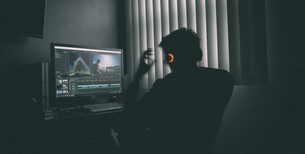 Persona con auriculares editando vídeo en un ordenador en una habitación a oscuras