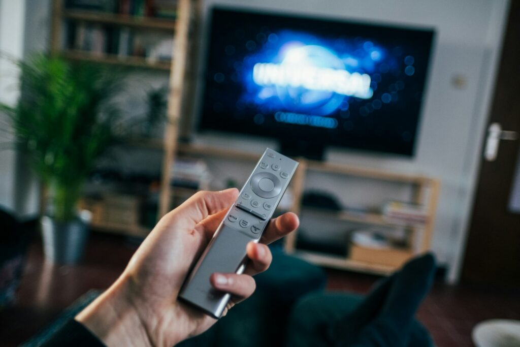Mano con un mando a distancia frente a un televisor en un salón