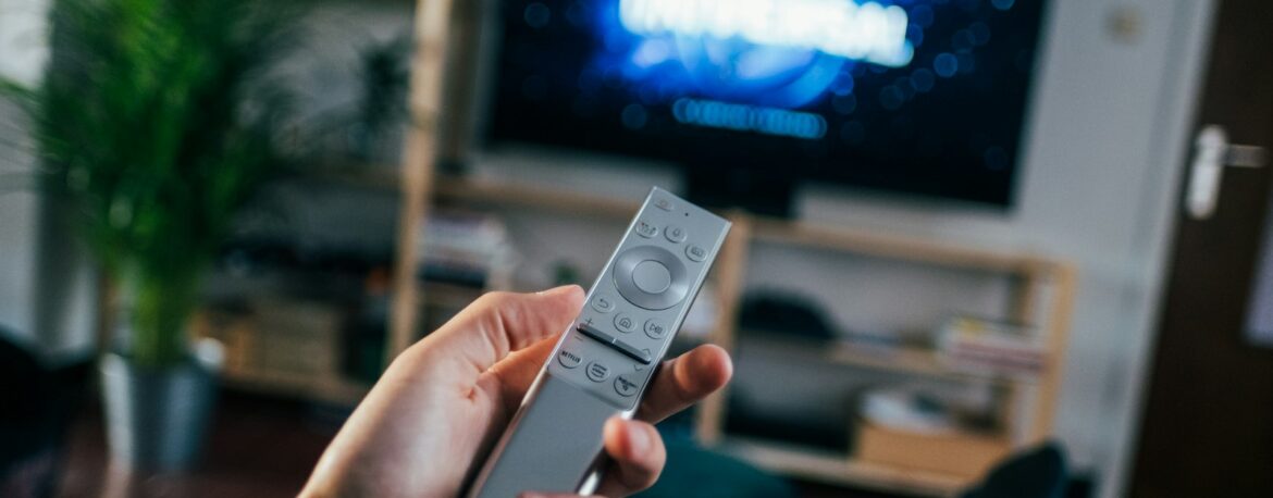 Mano con un mando a distancia frente a un televisor en un salón