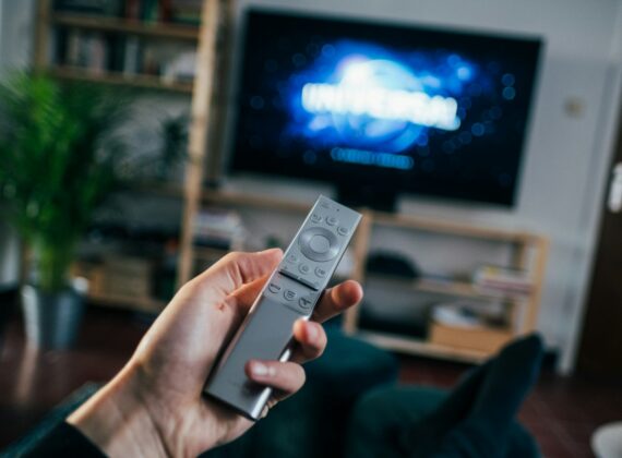 Mano con un mando a distancia frente a un televisor en un salón