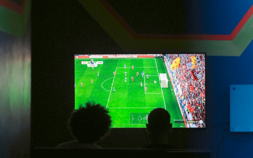 Dos personas viendo un partido de fútbol en el televisor de su casa