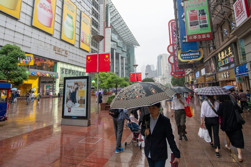Calle comercial de Shanghái con grandes pantallas publicitarias y peatones con paraguas bajo la lluvia