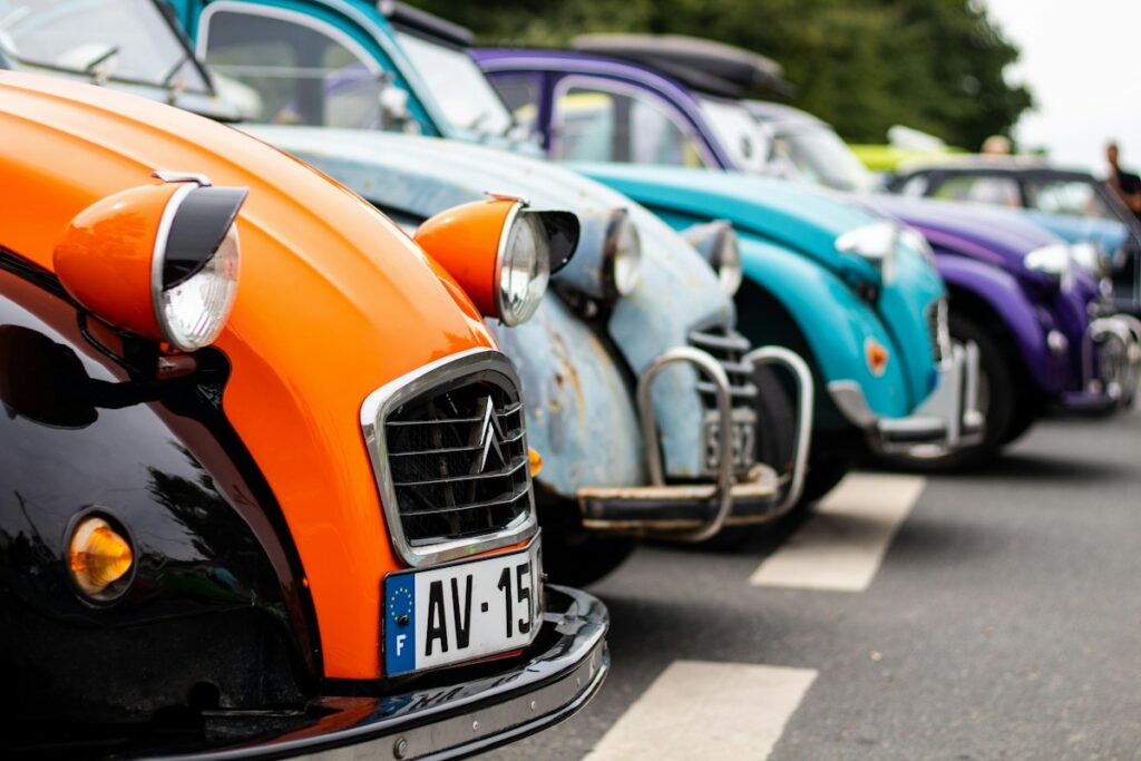 Fila de Citroën 2 CV clásicos de colores naranja, azul y morado aparcados