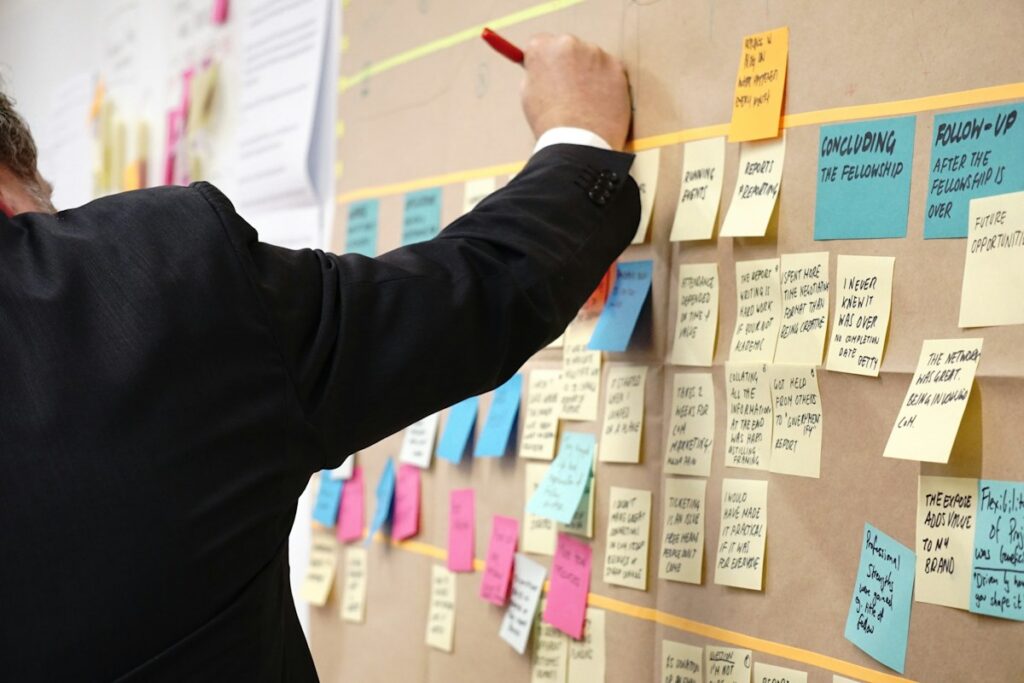 Persona colocando notas adhesivas de colores en un tablero de corcho organizado por columnas