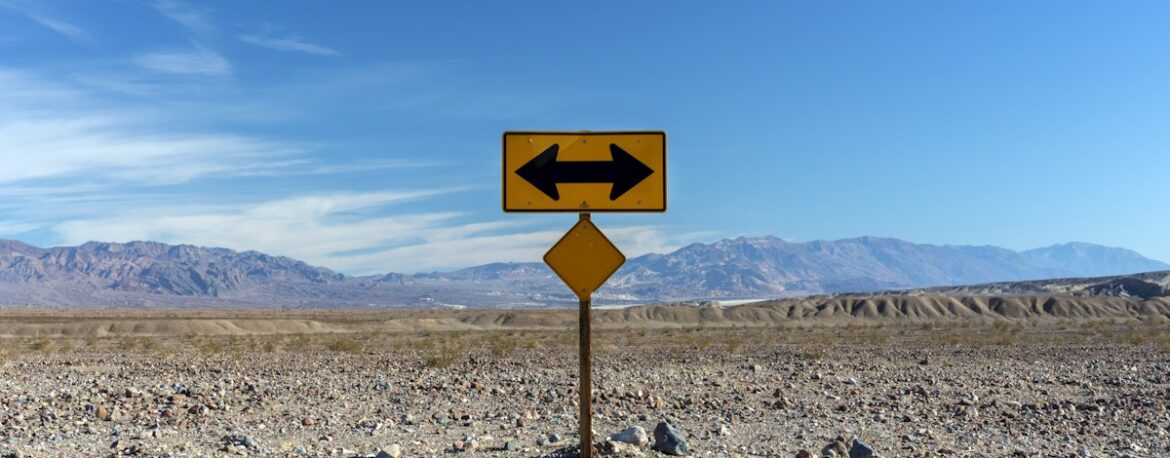 Señal de tráfico con una flecha que apunta en dos direcciones opuestas en una carretera del desierto