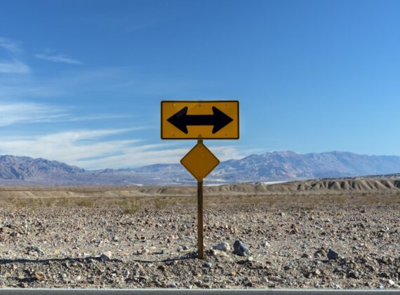Señal de tráfico con una flecha que apunta en dos direcciones opuestas en una carretera del desierto
