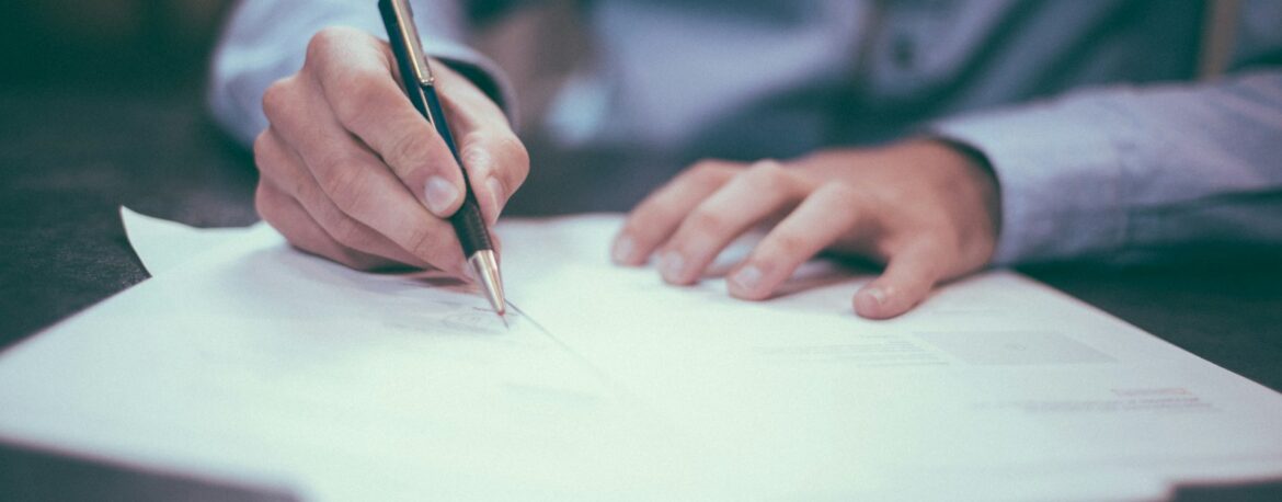 Manos firmando un documento sobre una mesa de reunión