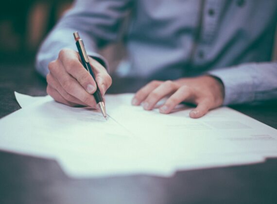 Manos firmando un documento sobre una mesa de reunión