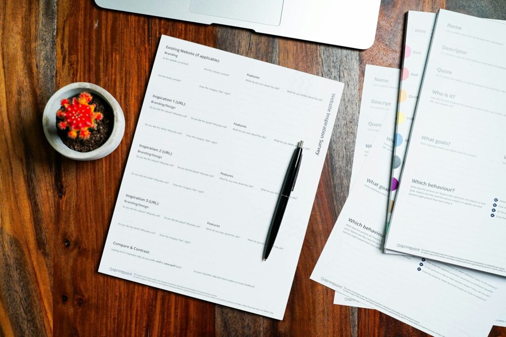 Formularios impresos y un bolígrafo sobre una mesa de madera junto a una planta