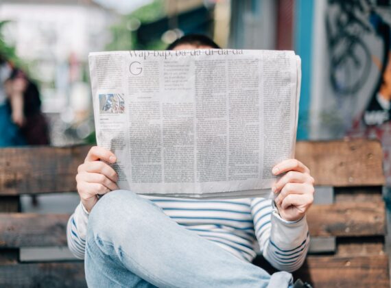 Hombre sentado en la calle leyendo un periódico desplegado