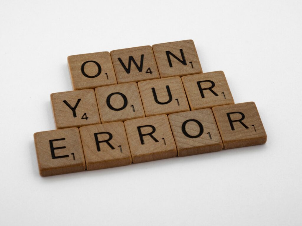 Fichas de un juego de letras que forman las palabras own your error sobre una mesa blanca