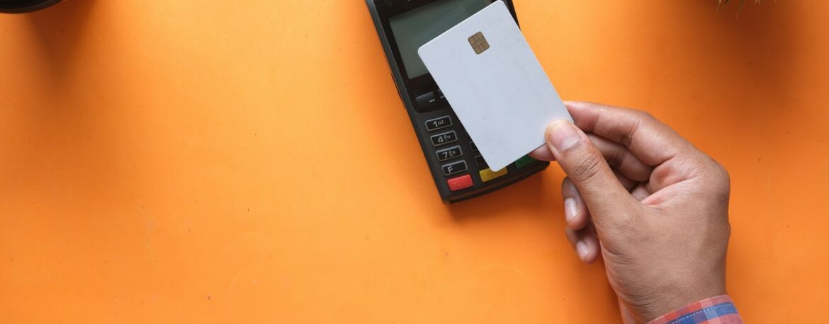 Una mano acerca una tarjeta a un datáfono sobre un fondo naranja