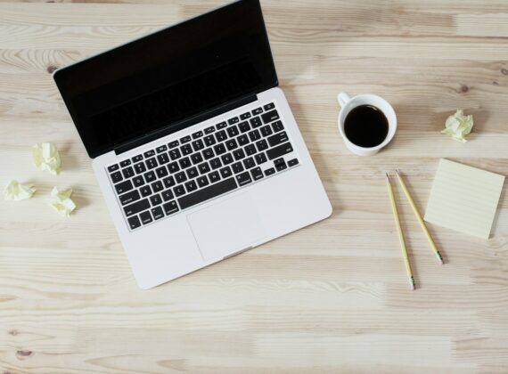 Portátil abierto junto a una taza de café y papeles sobre un escritorio claro
