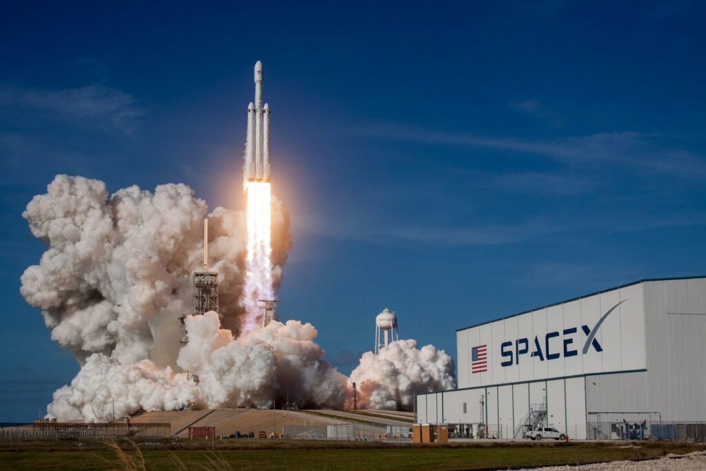 Despegue del cohete Falcon Heavy de SpaceX junto a un hangar con el logotipo de la empresa